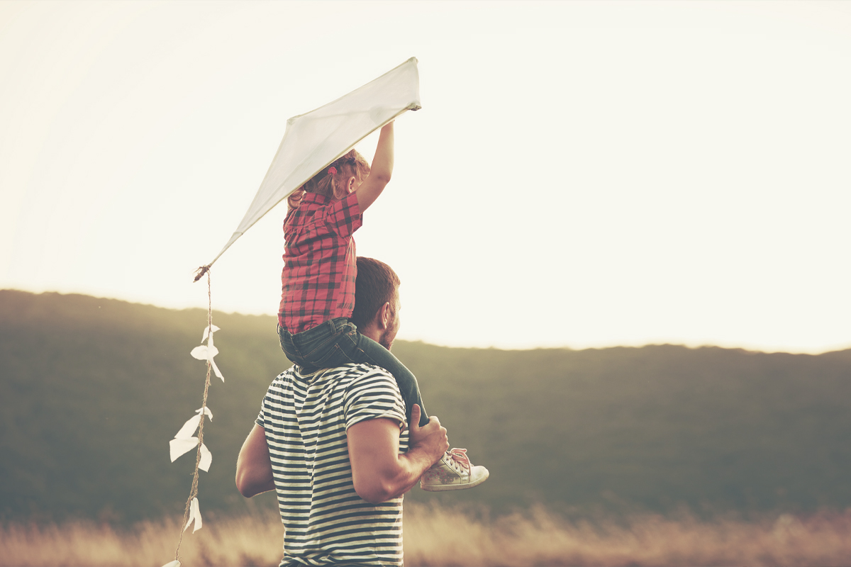 Photo of child with kite on man's shoulders